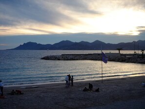 A beach with a rocky breakwater, calm sea, and mountains in the background. - Cannes, 2 rooms Furnished 3 stars 10 mn from the Palais and the beach (Cannes)