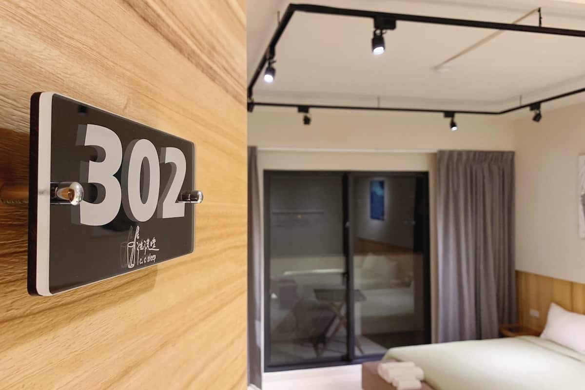 A hotel room with a large number sign, a sliding glass door, a bed, and a ceiling light fixture.