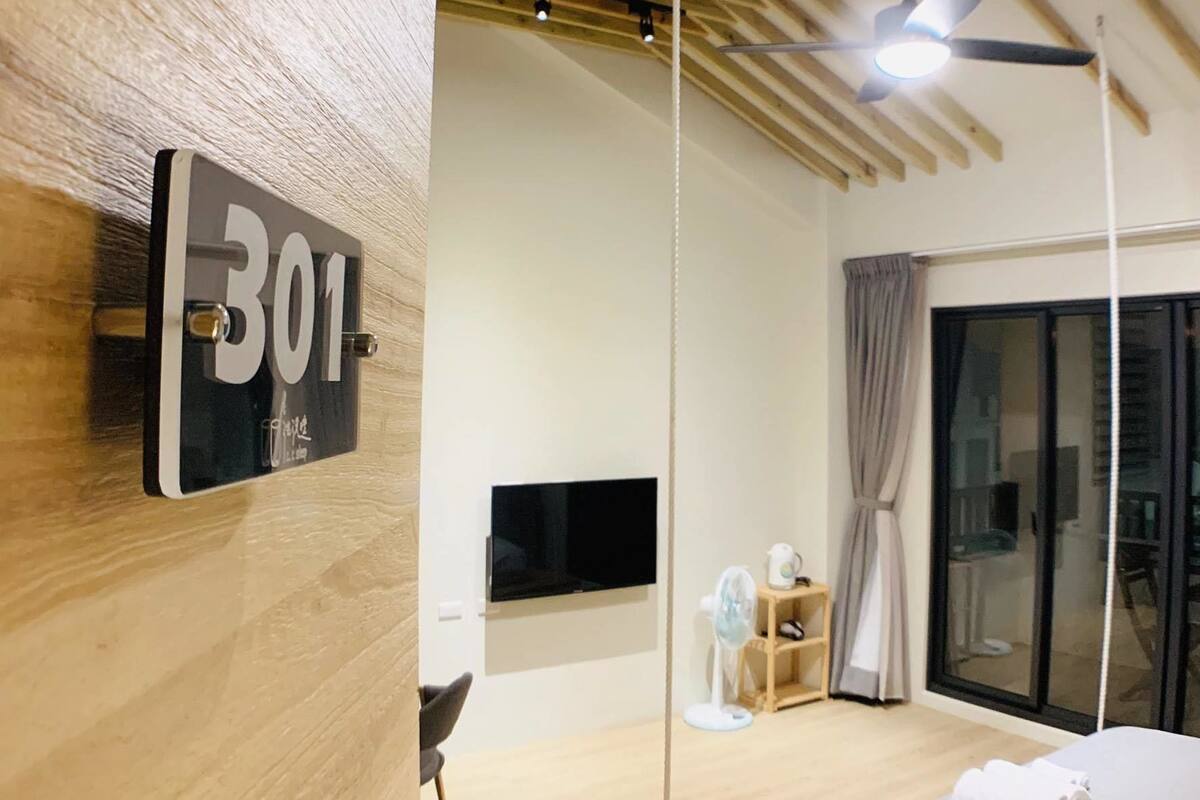 A modern hotel room with a wooden ceiling, a bed, a TV, and a window with curtains.