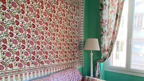 A room with a floral-patterned wall, a green wall, a window with curtains, a lamp, and a sofa with floral cushions. - Countryside in town, beautiful beach and all amenities  (Ajaccio)
