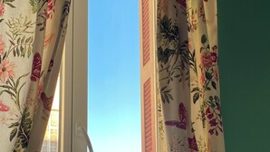 A window with floral curtains, a view of buildings, and a green wall. - Countryside in town, beautiful beach and all amenities  (Ajaccio)