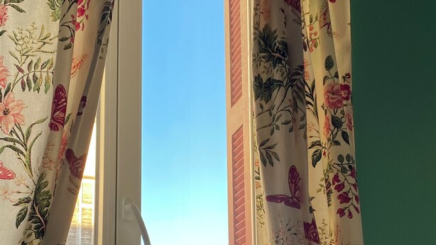 A window with floral curtains, a view of buildings, and a green wall. - Countryside in town, beautiful beach and all amenities  (Ajaccio)