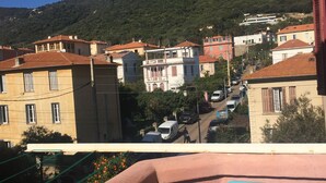 A balcony with a view of a residential street, houses, and a hill in the background. - Countryside in town, beautiful beach and all amenities  (Ajaccio)
