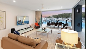 Una sala de estar moderna con televisor, asientos y vista a un puerto deportivo.