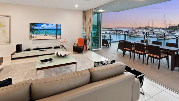 Un salón moderno con un televisor grande, asientos cómodos y vista a un puerto deportivo.