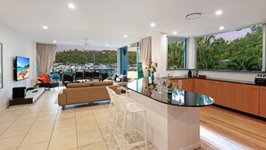 Una cocina moderna con barra, zona de estar con sofá y sillones, y un ventanal con vistas a un puerto deportivo.