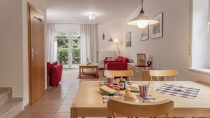 Un comedor con una mesa de madera, sillas y un sofá rojo. Hay una ventana con cortinas, una lámpara y un radiador.