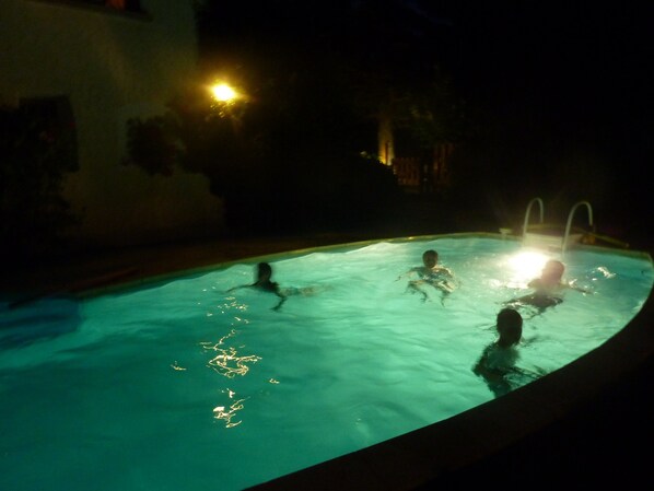 Piscina à noite com pessoas na água, iluminada por luzes subaquáticas.