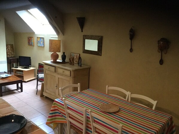 Un comedor con mantel a rayas, sillas blancas y un televisor al fondo.