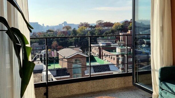 Ein Balkon mit Blick auf eine Stadtlandschaft, ein grünes Sofa, ein kariierter Stuhl und ein kleiner Tisch mit einem Buch.