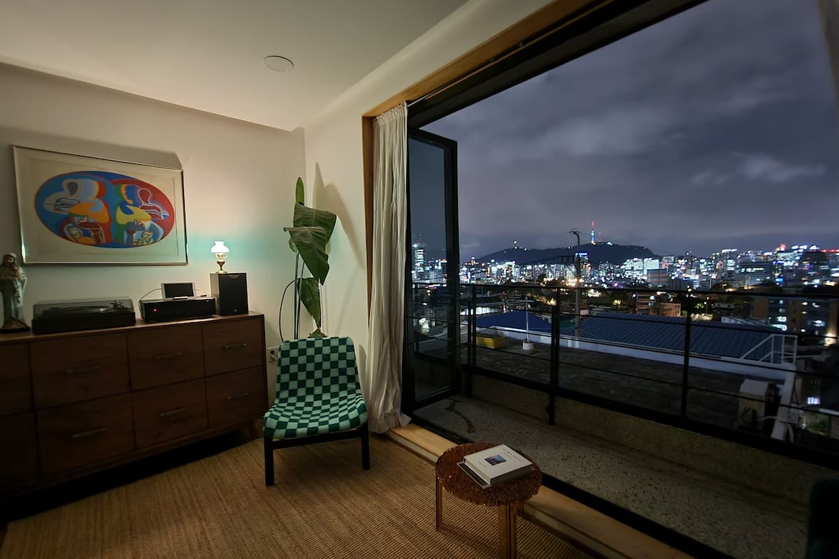 A modern hotel room with a large window overlooking a cityscape at night.