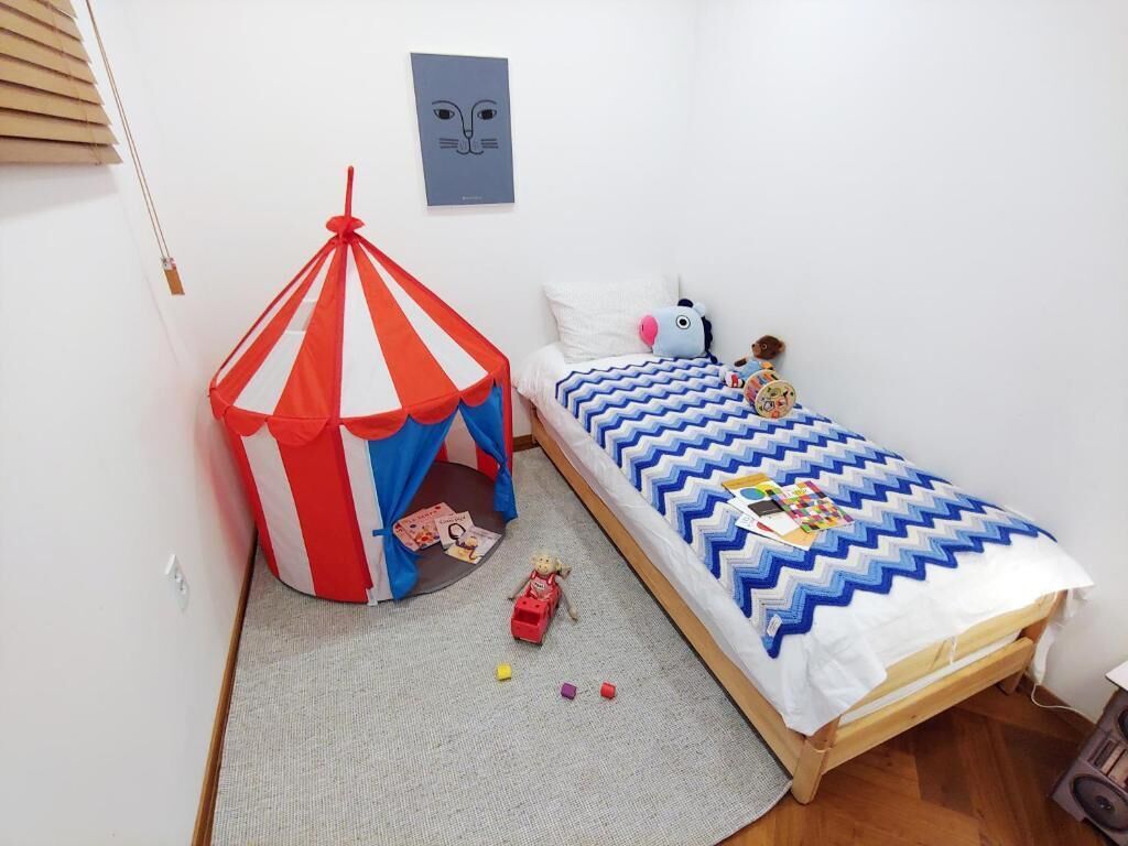 A bedroom with a bed, a small play area with a tent, and a wall with a picture.