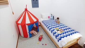 A bedroom with a bed, a small play area with a tent, and a wall with a picture.