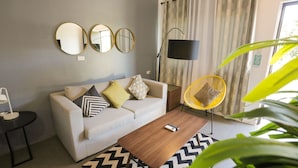 A modern living room with a sofa, a coffee table, a yellow chair, and three wall mirrors. - Treetop Suites (Coron)