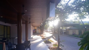 An outdoor seating area with chairs and tables, a covered walkway, and a view of a street with buildings and trees. - Treetop Suites (Coron)