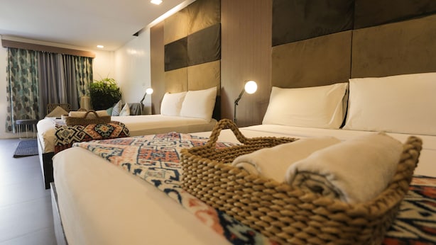 A modern hotel room with a large bed, a smaller sofa, and a desk. There are two bedside lamps and a plant in the corner. - Treetop Suites (Coron)