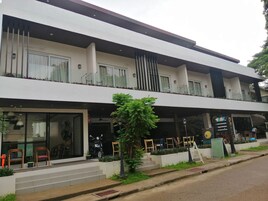 Un edificio moderno de dos pisos con techo plano, ventanas grandes y un balcón con barandas de vidrio.