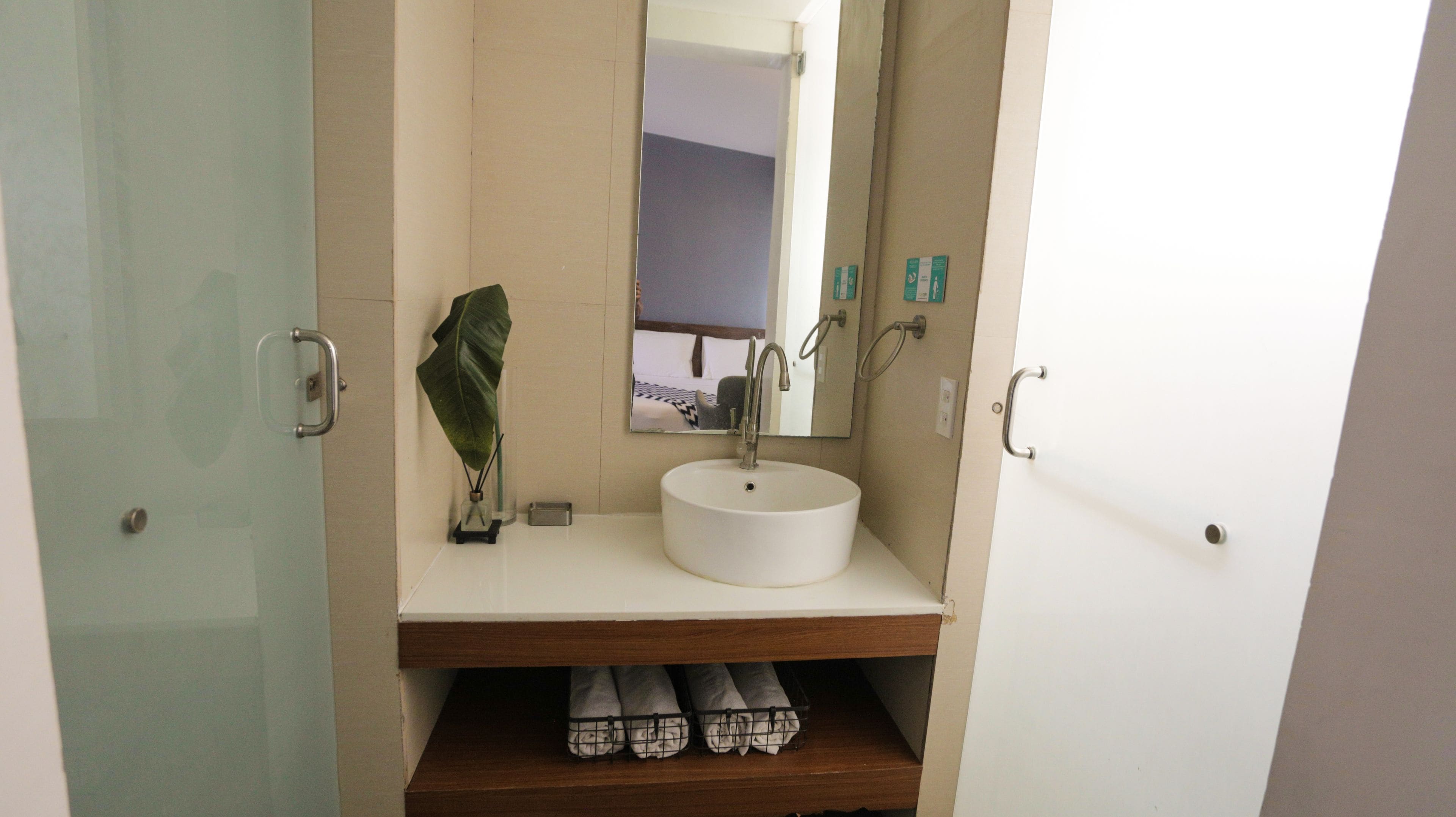 A bathroom with a white sink, a mirror, a shower, and a shelf with folded towels.