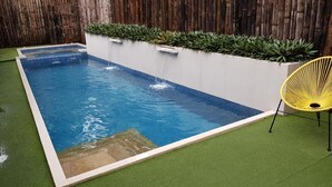 A rectangular swimming pool with a waterfall feature, surrounded by artificial grass and a bamboo fence. - Treetop Suites (Coron)