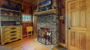 Una habitación rústica con chimenea de piedra, paredes de madera, un aparador de madera y una puerta de madera grande.
