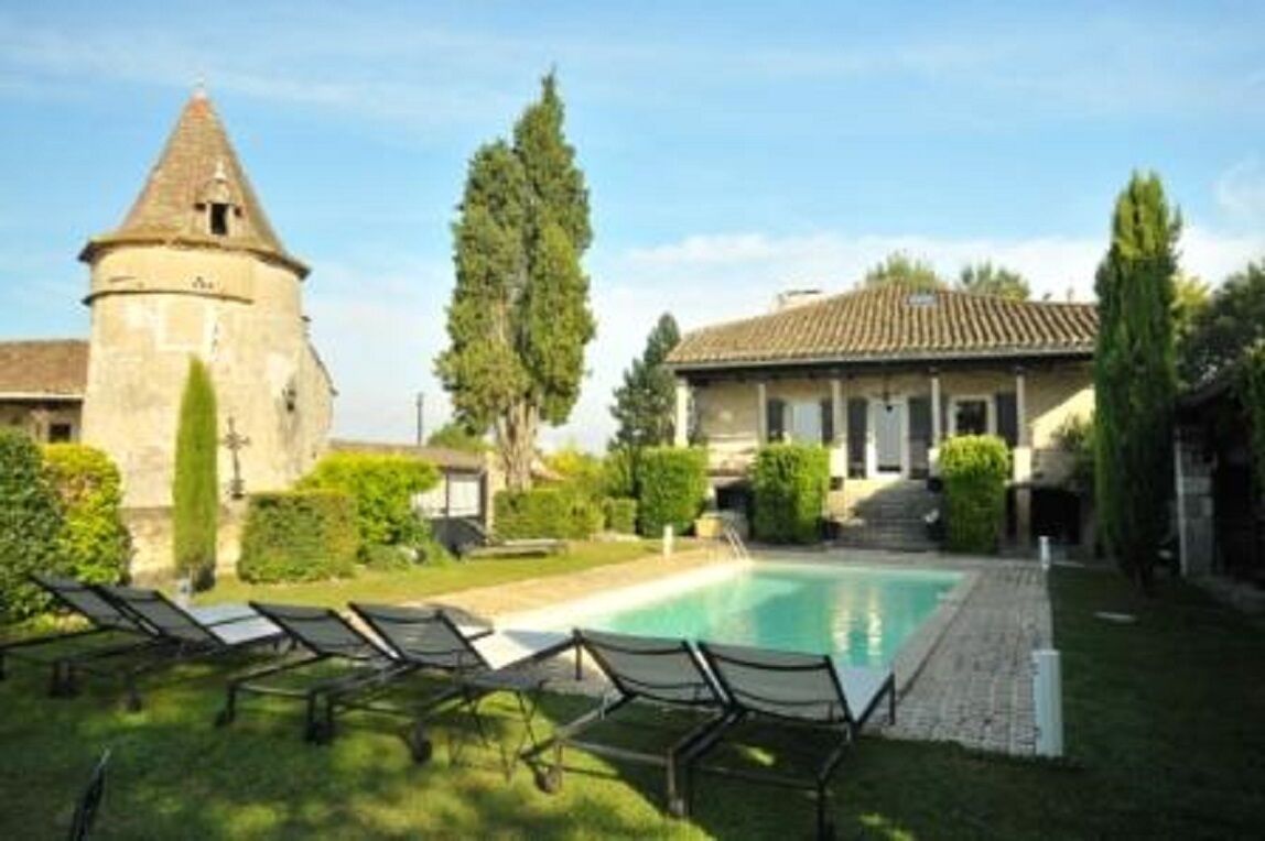 Un patio con piscina, sillas de descanso, una torre y un edificio con tejado de azulejos.