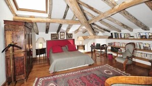 Un dormitorio con techo inclinado, vigas de madera, una cama con almohadas rojas, una estantería y un escritorio.