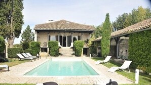 Zona junto a la piscina con una casa de piedra, sillones de descanso y una piscina cristalina.