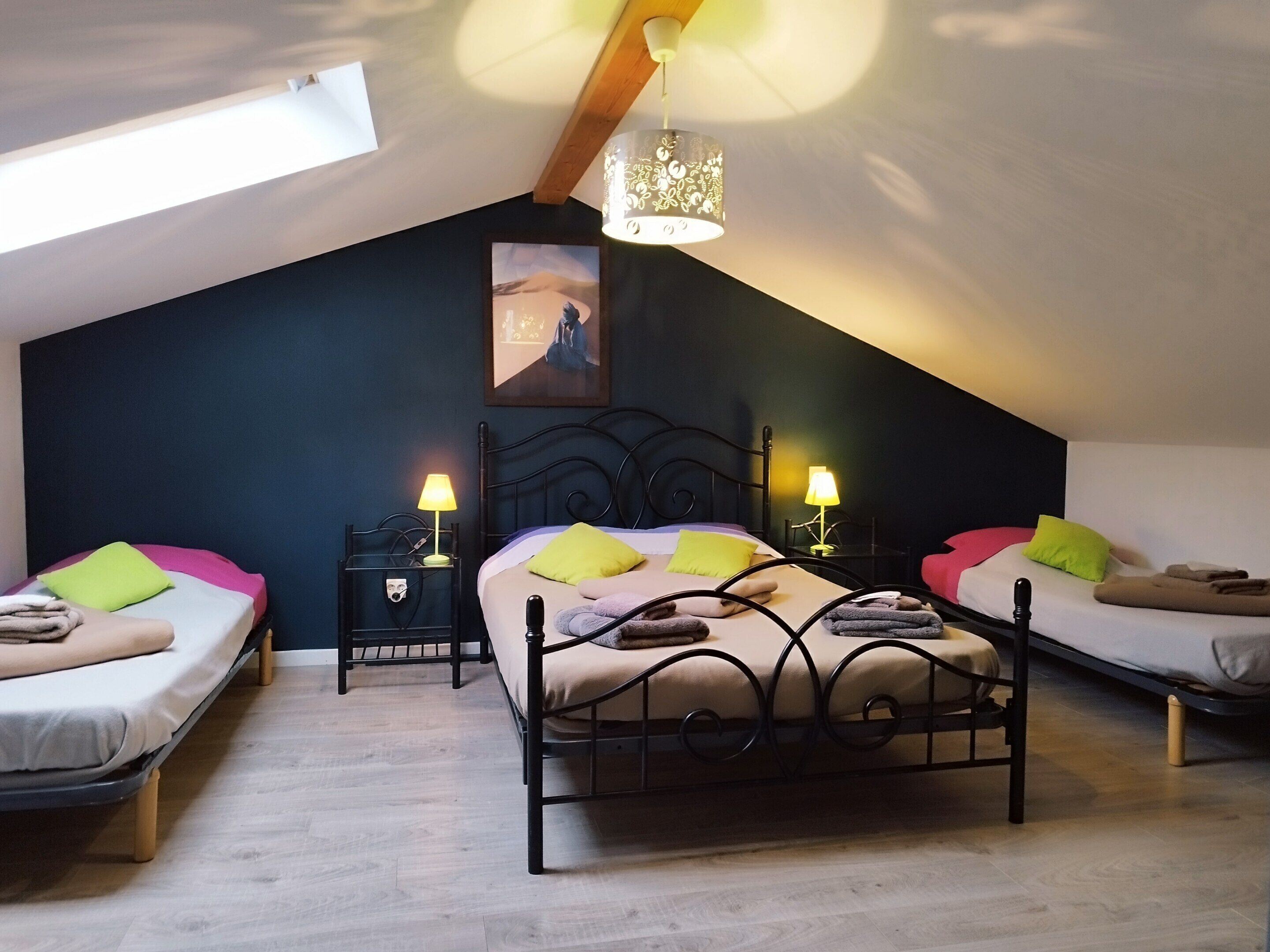 Ein gemütliches Schlafzimmer im Dachgeschoss mit schrägen Wänden, einem großen Bett mit Kopfteil, zwei Nachttischen mit Lampen und einem Gemälde an der Wand.