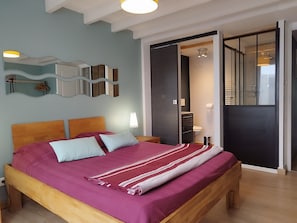 Une chambre avec un lit en bois, un grand miroir et une vue sur la salle de bain.