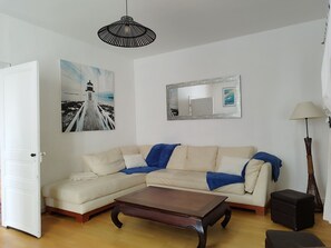 A living room with a sectional sofa, a wooden coffee table, a black hanging light fixture, a framed picture of a lighthouse, and a floor lamp. - Villa-4 étoiles-Oversized-Whirlpool bath-Terrace (Angoulins)