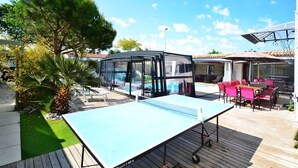 Un espacio exterior con mesa de ping pong, zona cubierta de cristal y piscina.