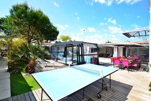 An outdoor area with a ping pong table, a glass-enclosed space, and a pool.