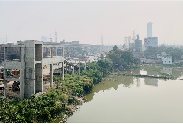 A construction site with a partially built structure, a river, and industrial buildings in the background. - Offbeat CCU on EM Bypass (Kolkata)