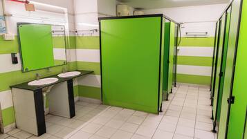 Baño con separadores verdes, pisos de baldosas blancas y dos lavamanos con encimeras negras.