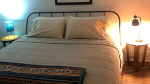 Una cama bien hecha con un edredón estampado, una obra de arte enmarcada encima y dos lámparas de noche.