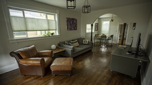 Amplia sala de estar con sofá de cuero, reposapiés y comedor con mesa y sillas.