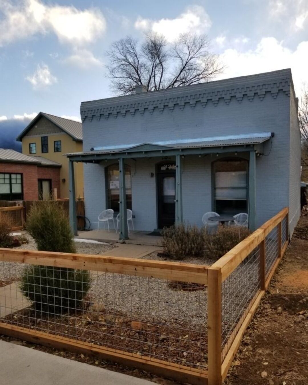 A small, single-story building with a porch and a fenced garden area.