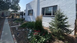 Una casa moderna de ladrillo blanco con una chimenea visible, un patio delantero con un sendero y un pequeño árbol.