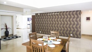 A dining area with a wooden table set for four, surrounded by chairs. A decorative wall with a floral pattern is behind the table. - SKYLA Serviced Apartments Banjara Hills (Hyderabad)