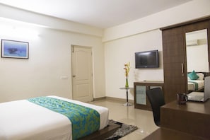 A hotel room with a bed, a desk, a chair, a TV, and a door. - SKYLA Serviced Apartments Banjara Hills (Hyderabad)