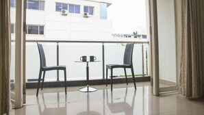 A balcony with two chairs and a small table, a view of a building with air conditioning units, and a curtain on the right. - SKYLA Serviced Apartments Banjara Hills (Hyderabad)