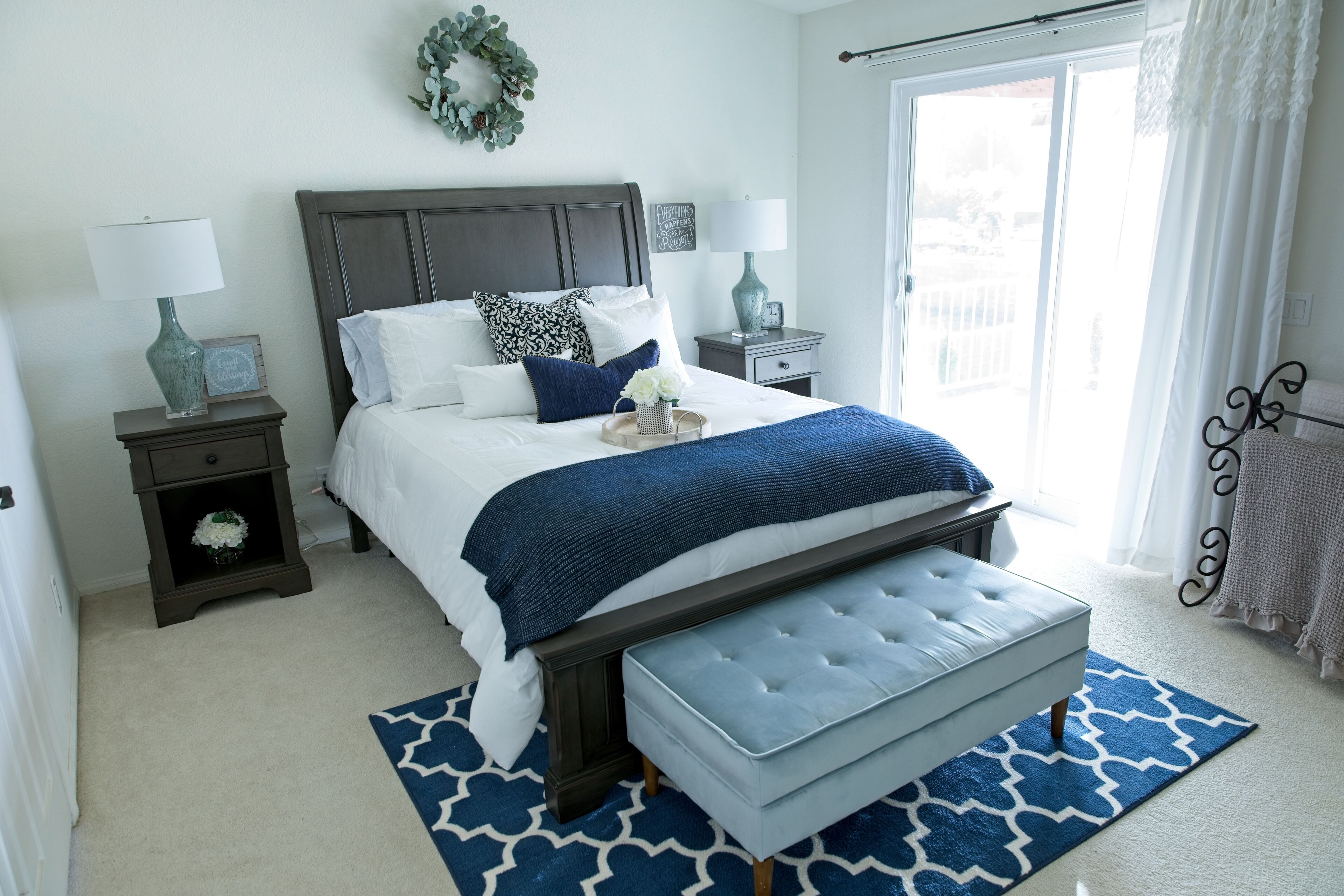 A bedroom with a bed, nightstands, a bench, and a view of the outdoors.