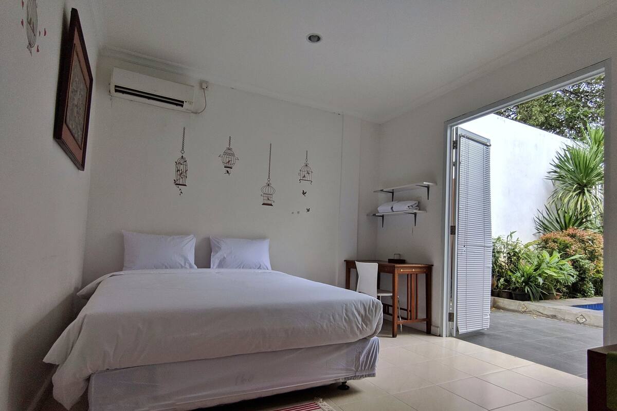 Un dormitorio con cama, una mesita de noche pequeña, una silla y un aire acondicionado instalado en la pared.