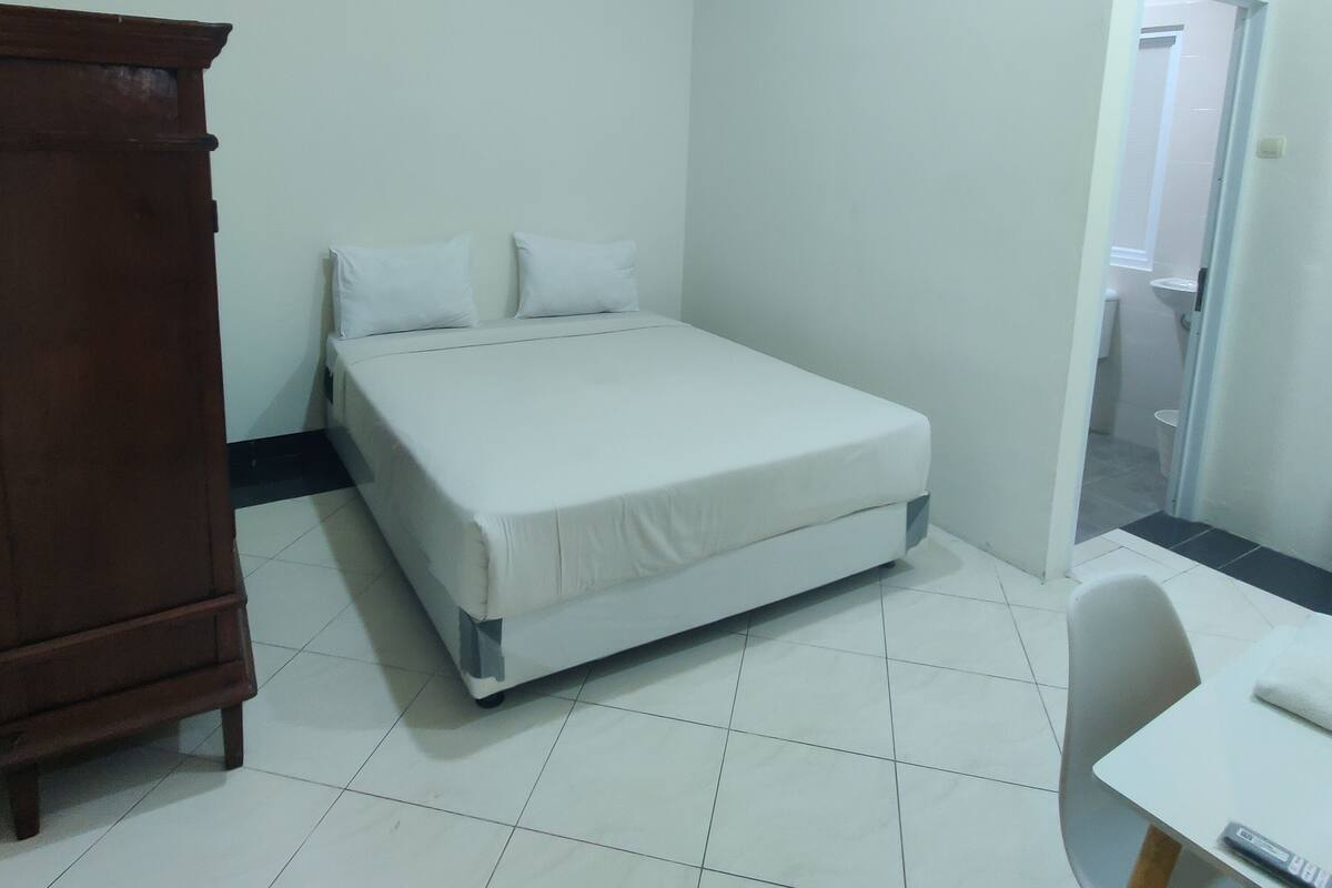 Una habitación pequeña y limpia con una cama individual, un armario de madera y un escritorio.