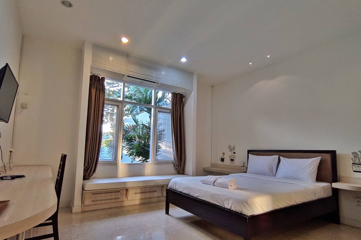 Un dormitorio con cama, escritorio y ventana con cortinas.