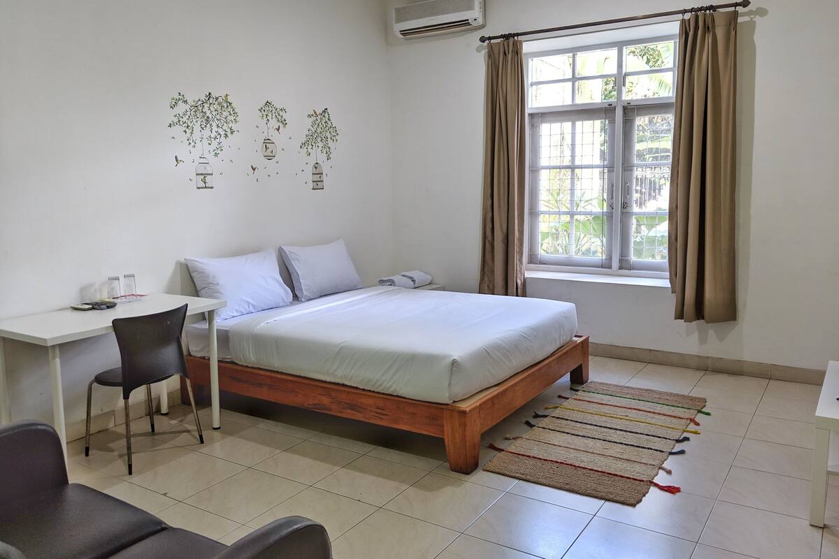 Un dormitorio con cama, escritorio, silla y ventana con cortinas.