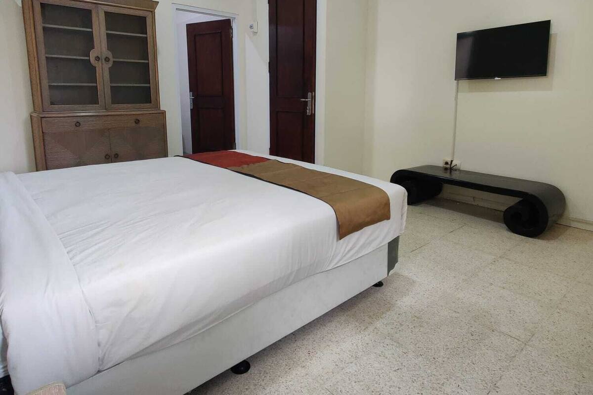 Un dormitorio con cama, un armario de madera, televisor y puerta.