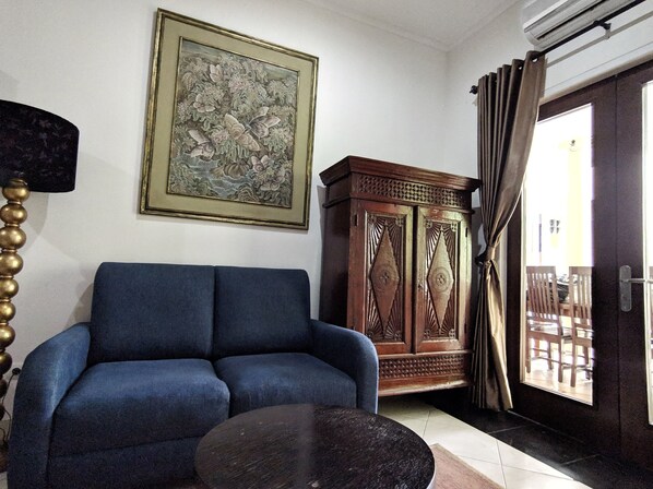 A living room with a blue sofa, a round coffee table, a wooden cabinet, and a framed floral artwork on the wall. - My Home by FLAT06 (Jakarta)
