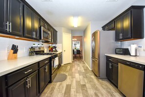 Equipped with an oven, microwave, and refrigerator, this kitchen offers a clean and minimalist design with a light wood floor.