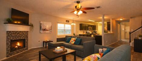 A cozy living room with a fireplace, a sofa, a coffee table, and a ceiling fan.